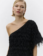 Woman wearing a black one-shoulder dress with fringe details on a white background