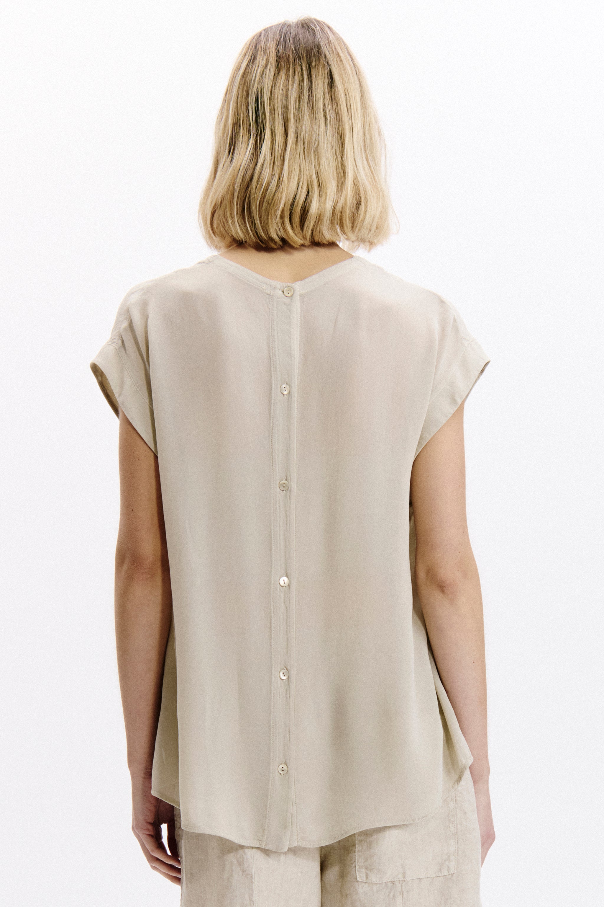 Person wearing a beige sleeveless top on a white background