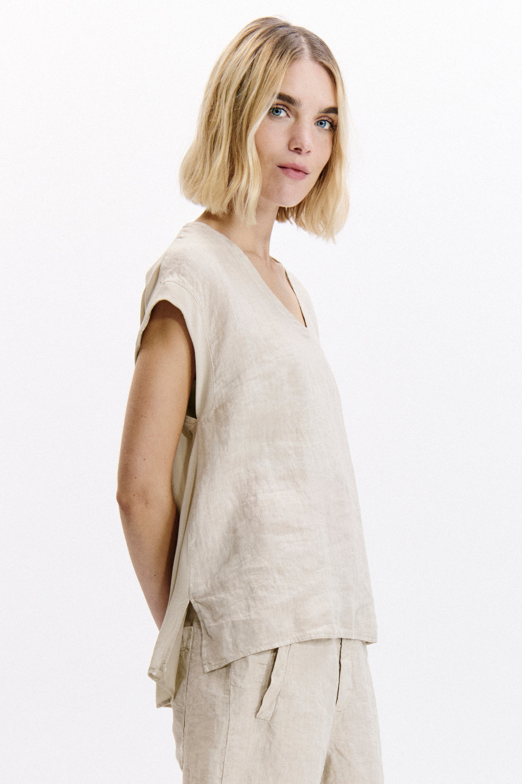 Woman wearing a beige sleeveless top and pants on a white background