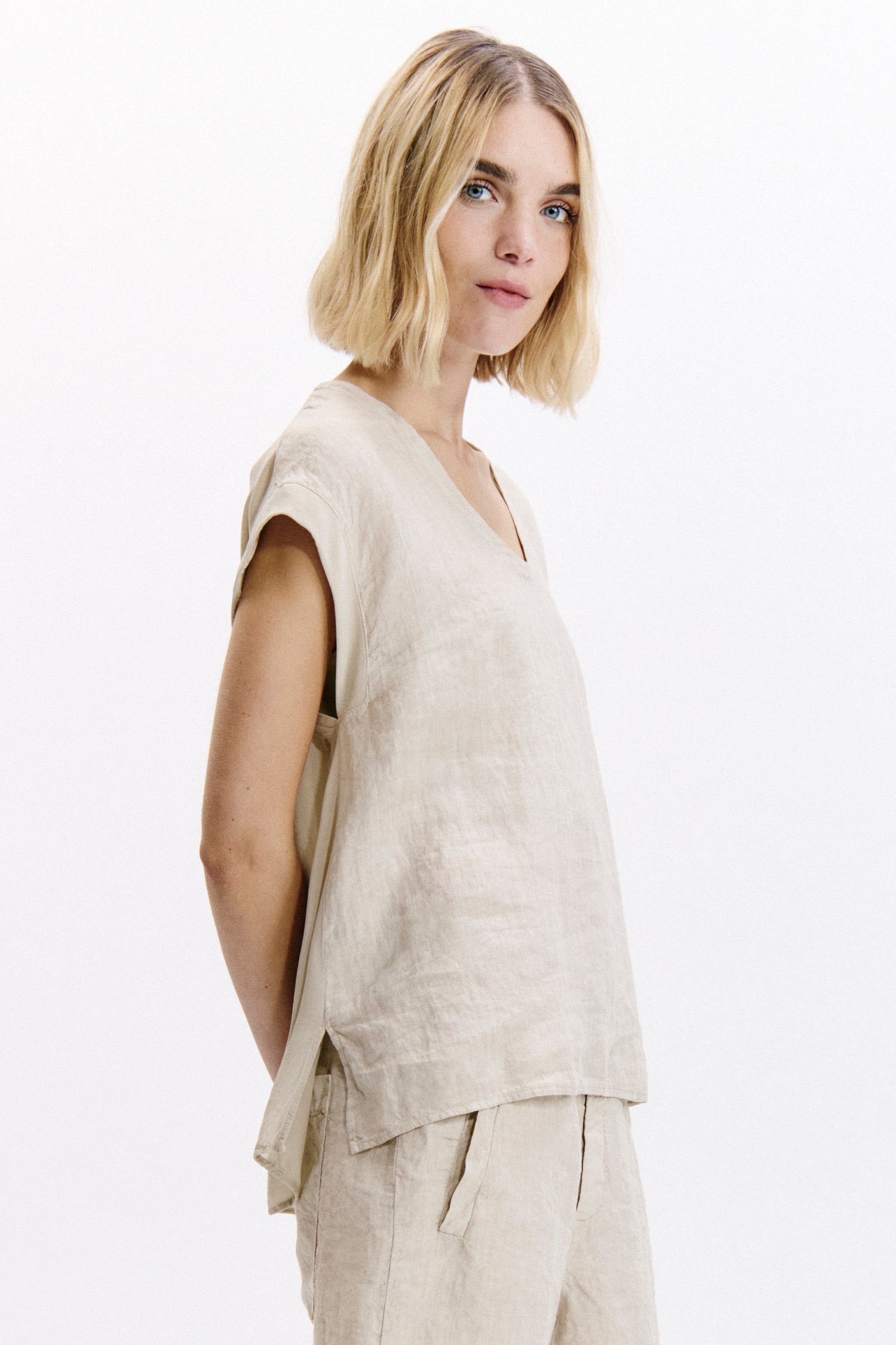 Woman wearing a beige sleeveless top and pants on a white background