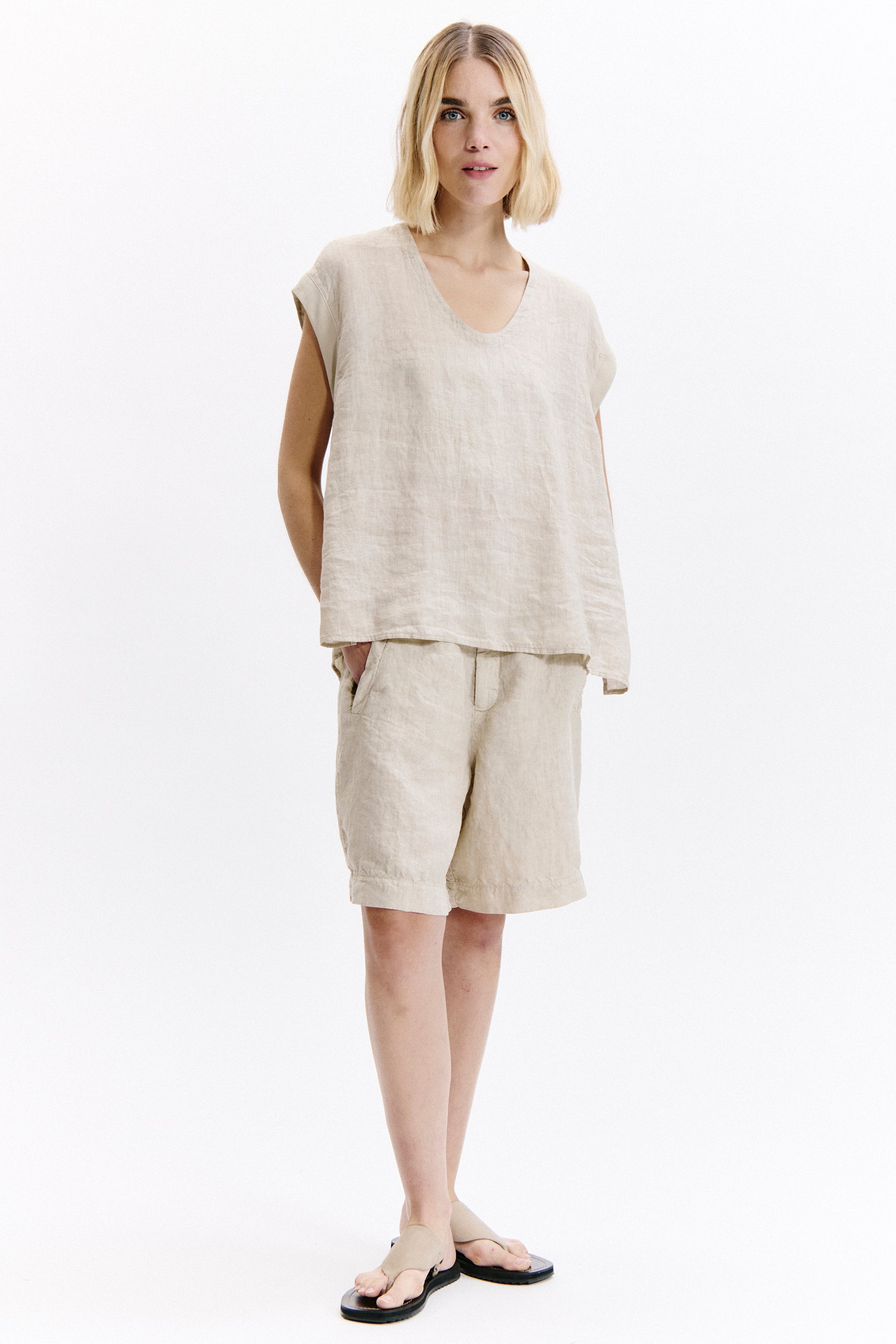 Woman wearing a beige sleeveless top and shorts on a white background