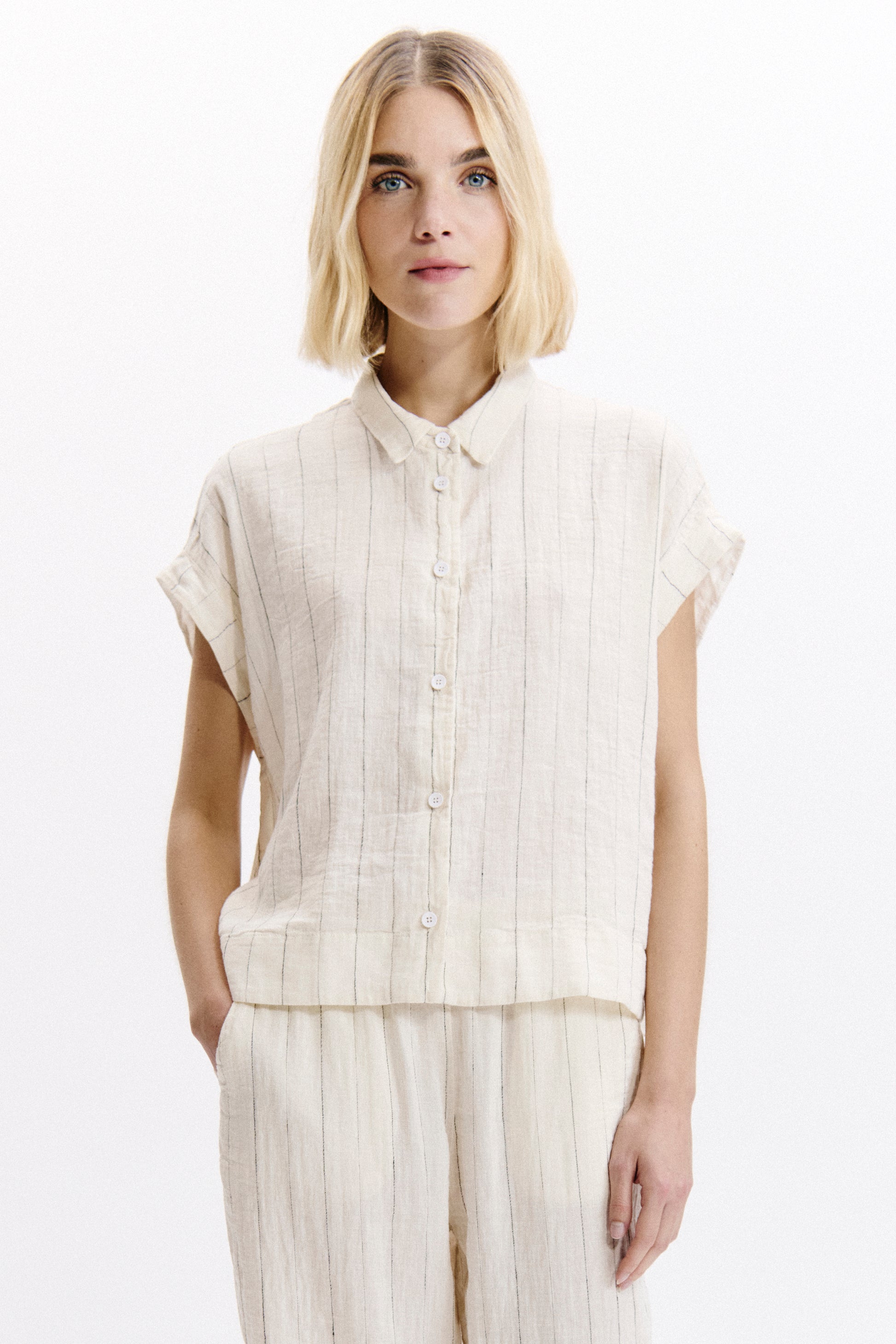 Woman wearing a sleeveless beige top and pants on a white background