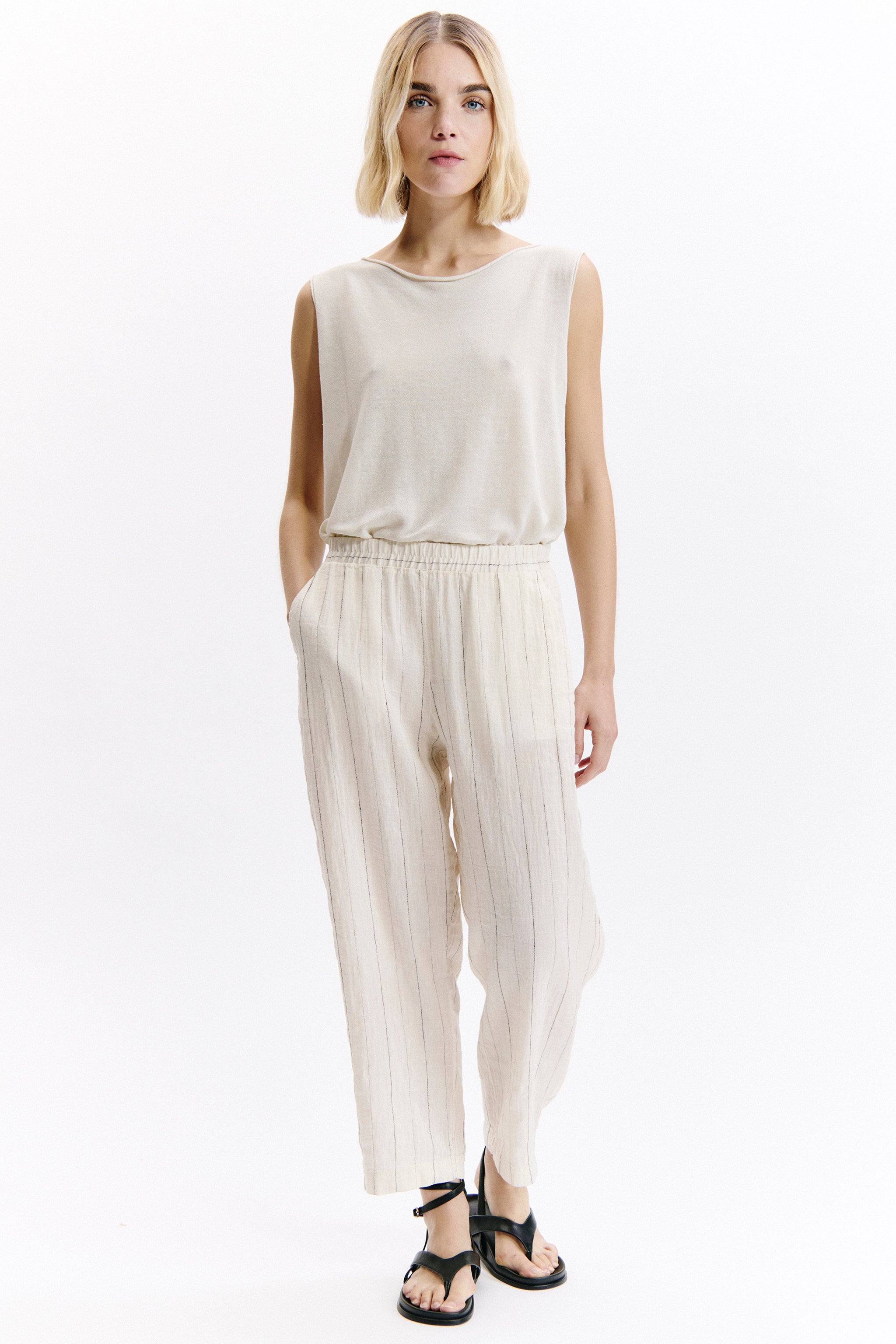 Woman wearing a white sleeveless top and high-waisted pants on a white background