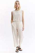 Woman wearing a white sleeveless top and high-waisted pants on a white background