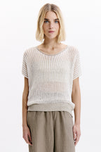Woman wearing a light-colored knitted top and beige pants on a white background