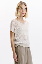 Woman wearing a light-colored knit top and beige pants on a white background