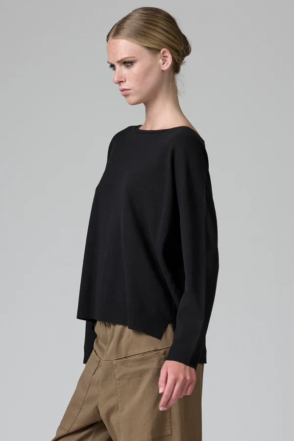 Woman wearing a black sweater and beige pants on a gray background