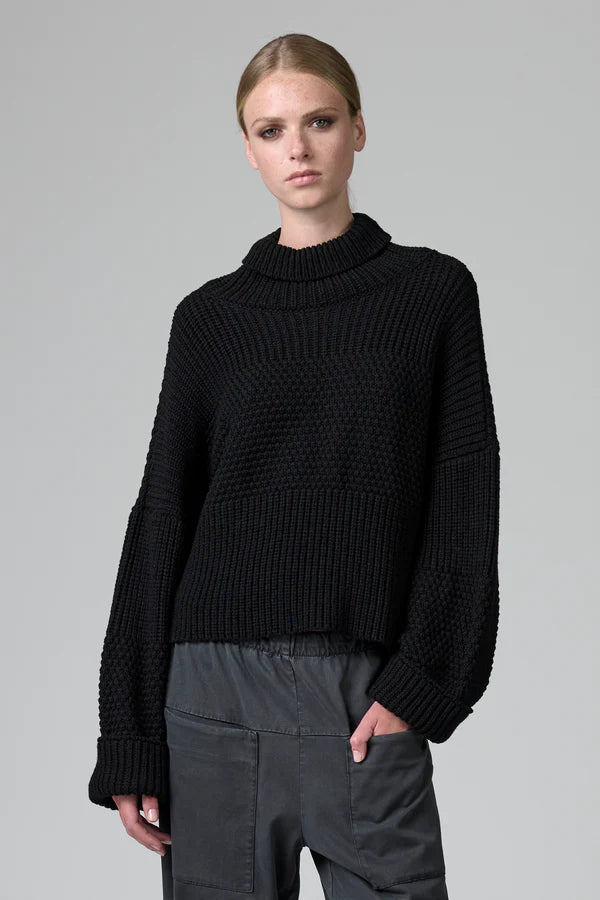 Person wearing a black ribbed sweater on a gray background