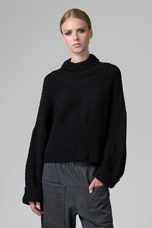Person wearing a black ribbed sweater on a gray background