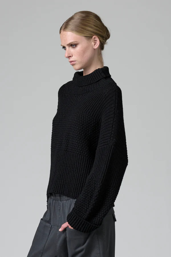 Woman wearing a black knitted sweater against a gray background