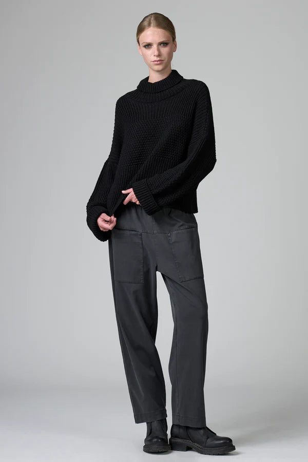 Person wearing a black sweater and gray pants on a plain background