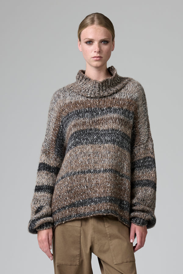 Model wearing a striped sweater and beige pants against a gray background