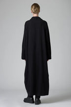 Person wearing a long black coat on a plain background