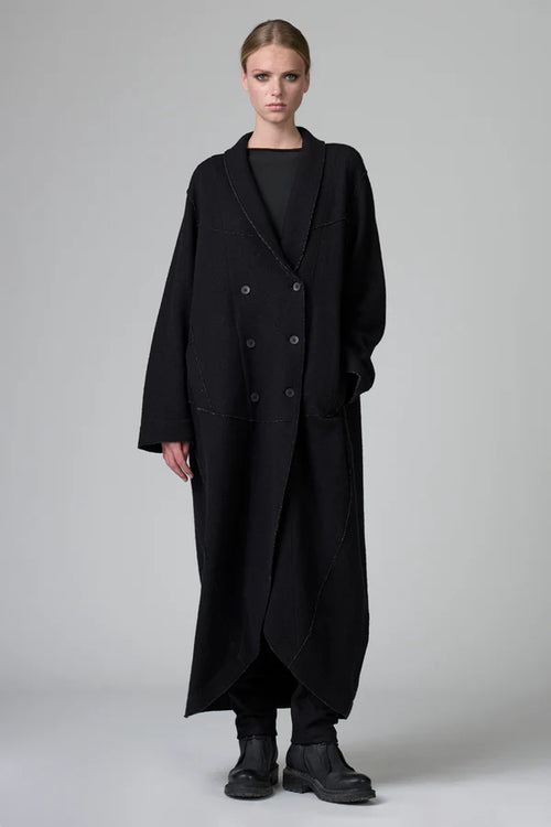 Person wearing a long black coat on a plain background