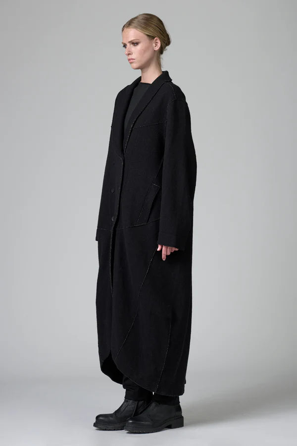 Person wearing a long black coat on a plain background