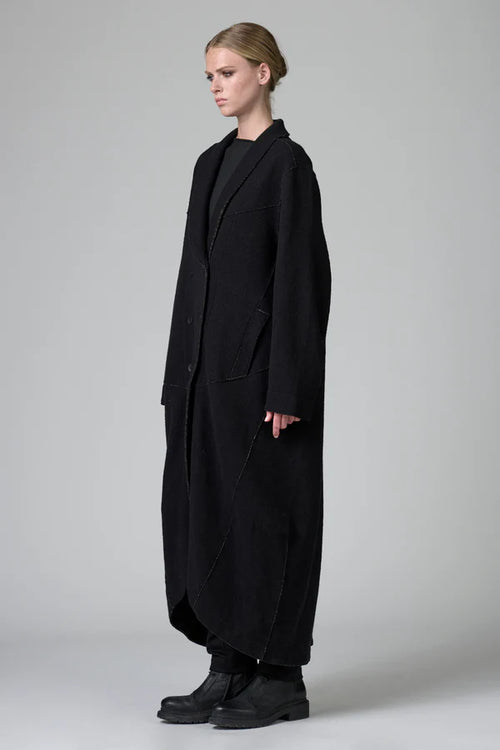 Person wearing a long black coat on a plain background