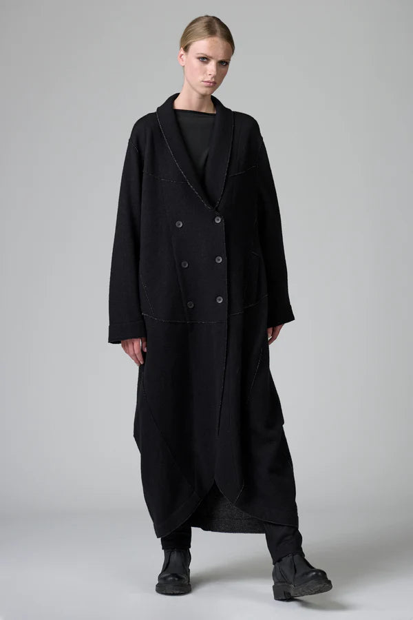 Person wearing a long black coat on a plain background