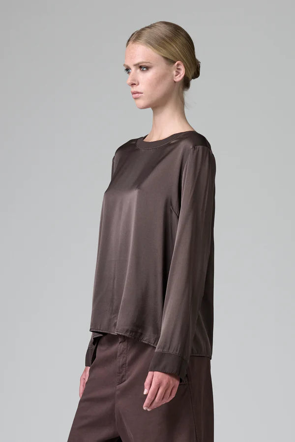 Woman wearing a brown long-sleeve top and pants on a gray background