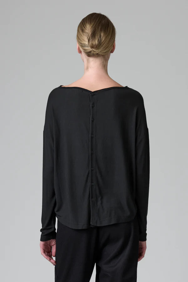 Person wearing a black long-sleeve top with a button detail on a gray background