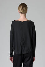 Person wearing a black long-sleeve top with a button detail on a gray background
