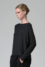 Woman wearing a black long-sleeve top against a gray background
