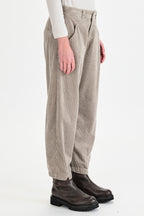 Person wearing beige pleated pants and dark boots on a white background