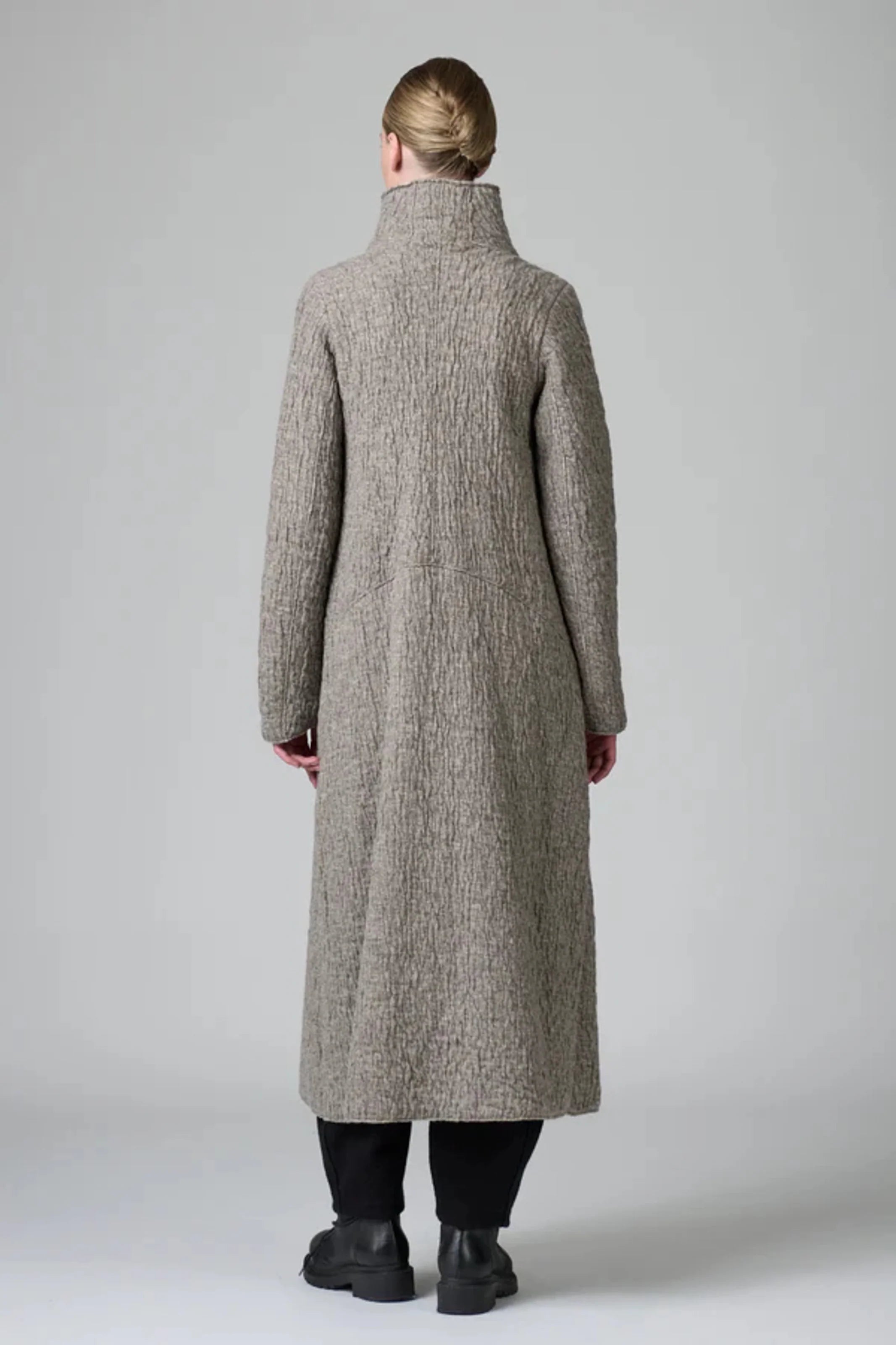 Person wearing a long gray coat on a plain background