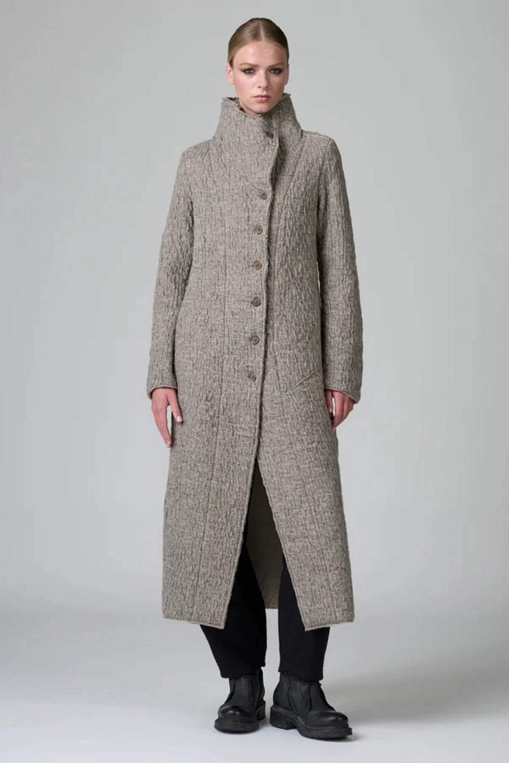 Woman wearing a long, textured coat on a plain background