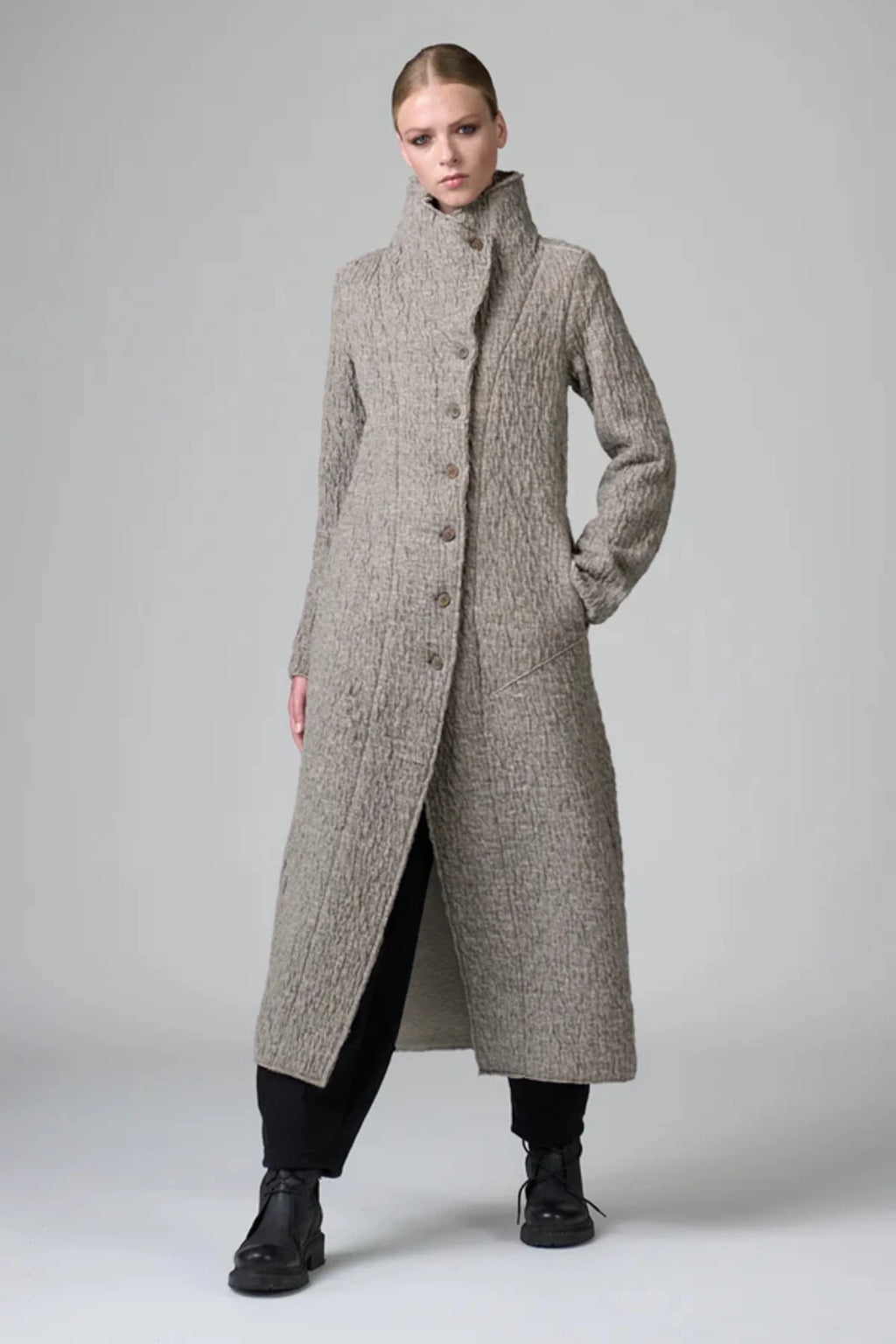Woman wearing a long, textured coat on a plain background