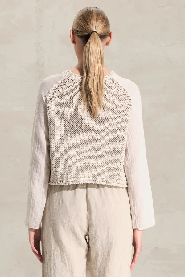 Person wearing a light-colored top with a textured pattern on a plain background
