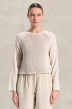 Woman wearing a light-colored knitted top and pants against a neutral background