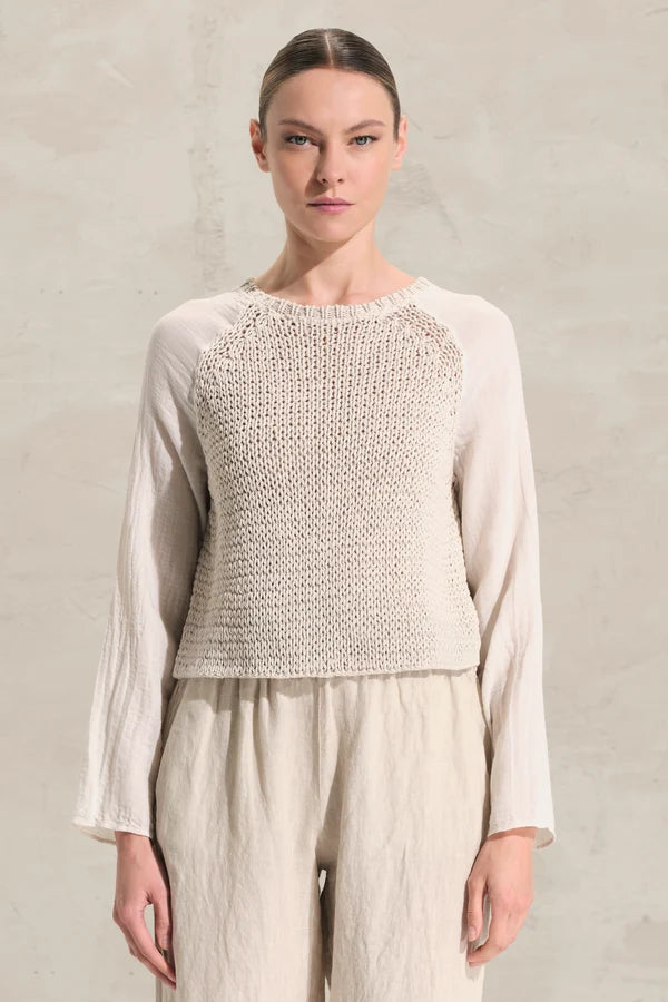 Woman wearing a light-colored knitted top and pants against a neutral background