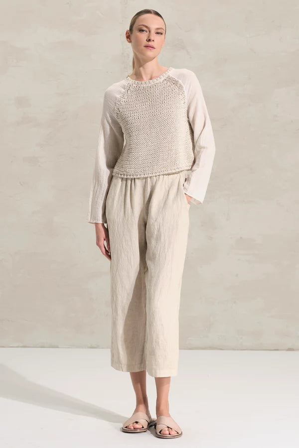 Woman wearing a light-colored knit top and wide-leg pants against a neutral background