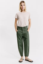 Person wearing a beige t-shirt and green pants on a white background