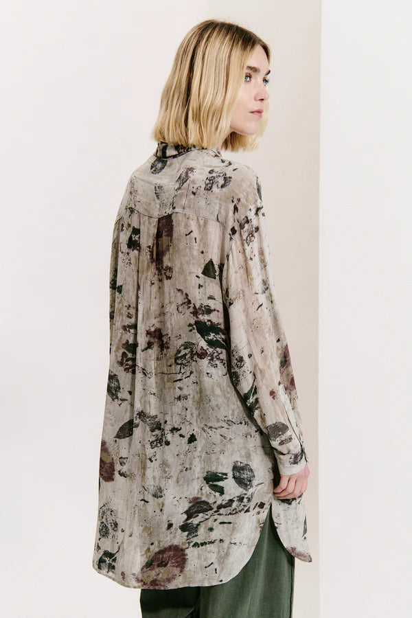 Woman wearing a long floral-patterned shirt against a plain background