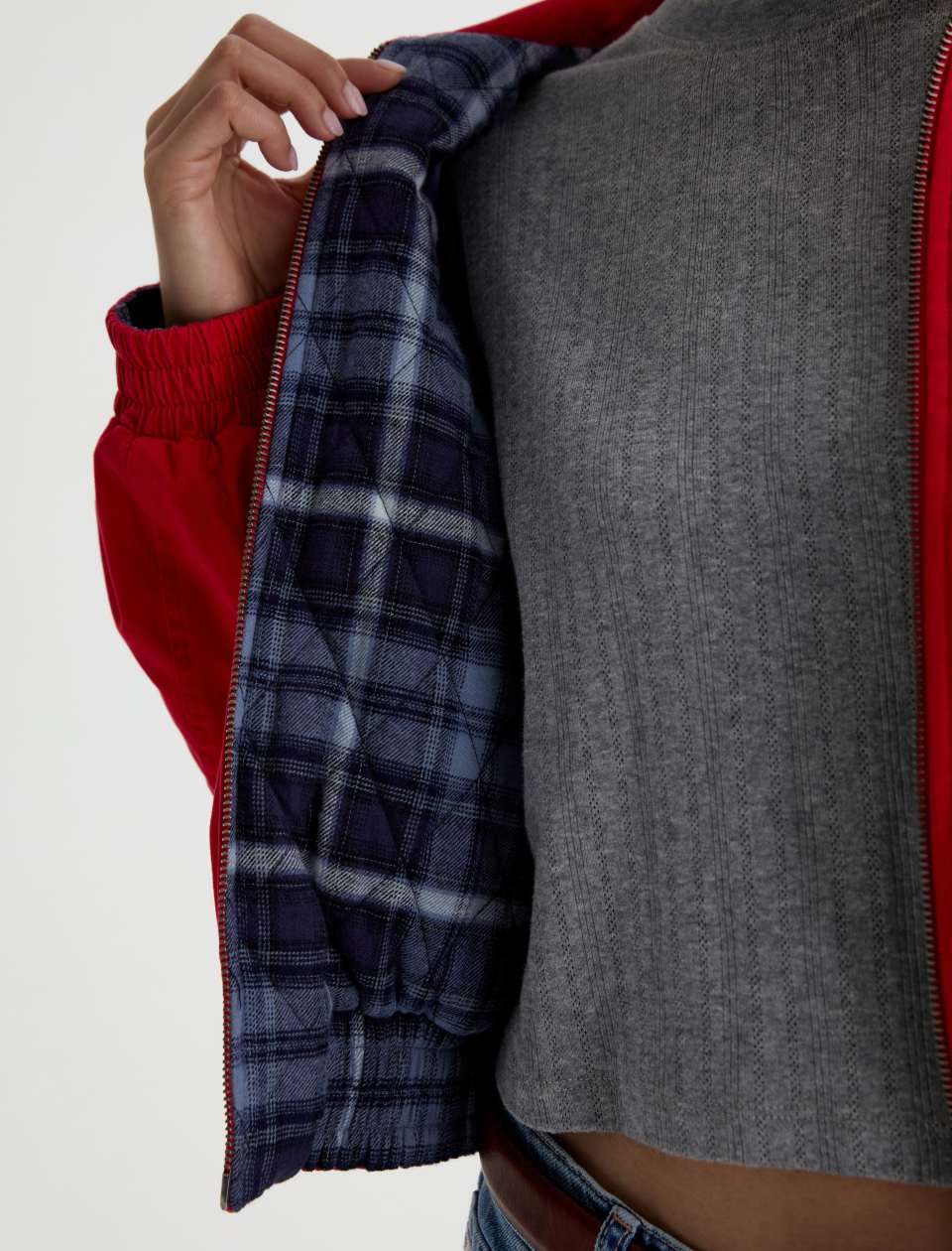 Close-up of a person wearing a red zip-front jacket with a gray knit top underneath and a navy plaid lining visible when the jacket is opened.