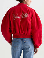 A person shown from the back wearing a bright red satin bomber jacket with 'Jazz Club' script and 'Los Angeles, Calif.' printed on the back, paired with blue jeans against a light gray studio background.