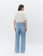 Woman wearing light blue jeans and a white top on a white background