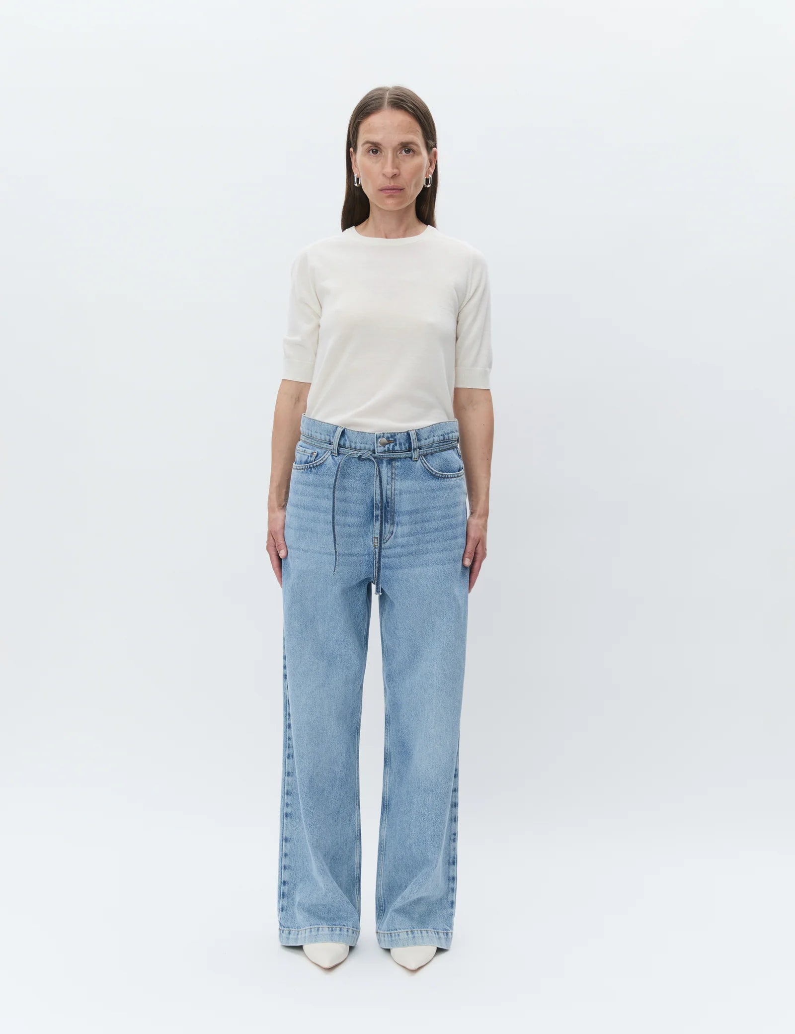 Woman wearing light blue jeans and a white top on a plain background