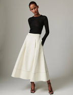 Woman wearing a black top and white skirt against a plain background