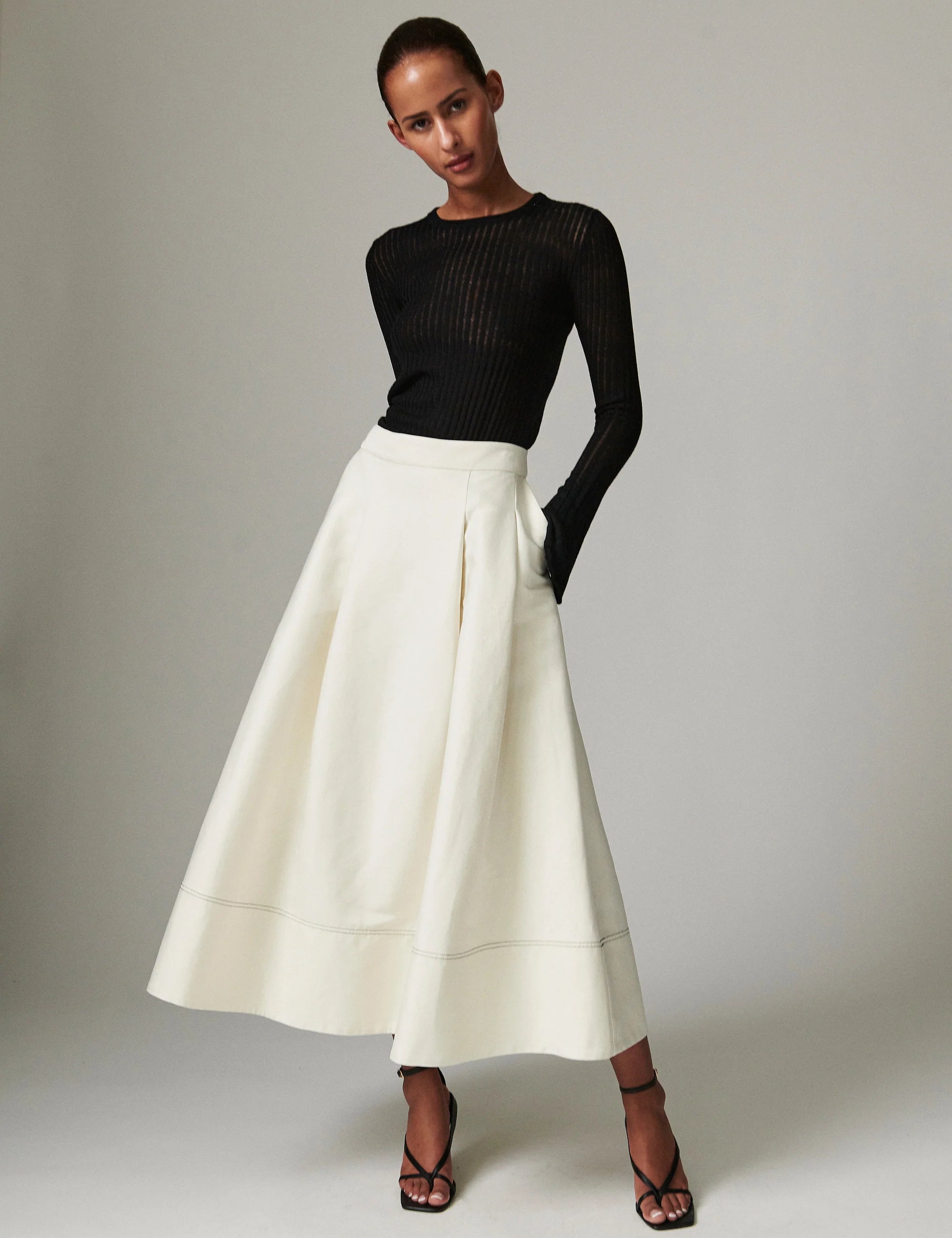 Woman wearing a black top and white skirt against a plain background