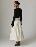 Woman wearing a black long-sleeve top and white skirt on a plain background