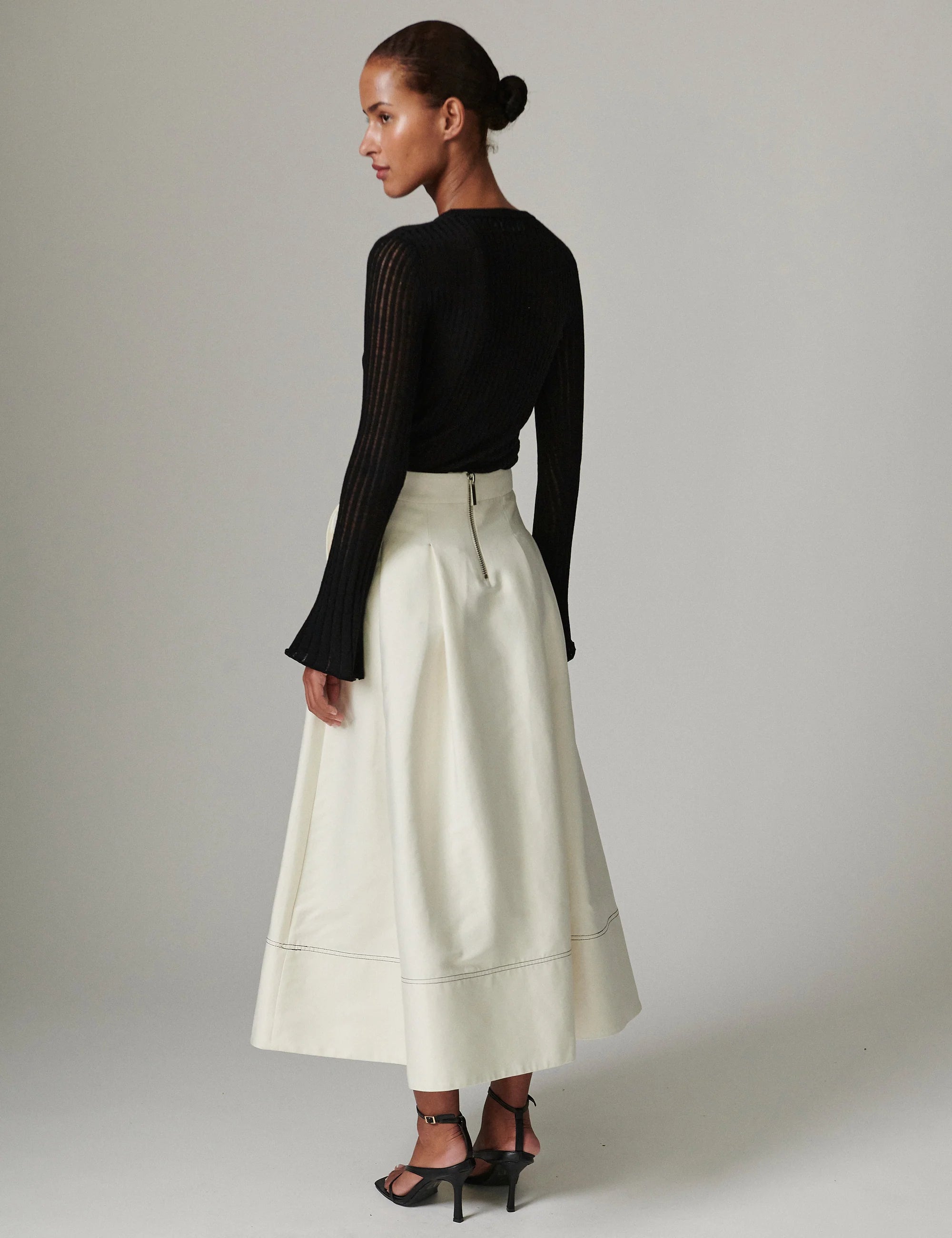 Woman wearing a black long-sleeve top and white skirt on a plain background