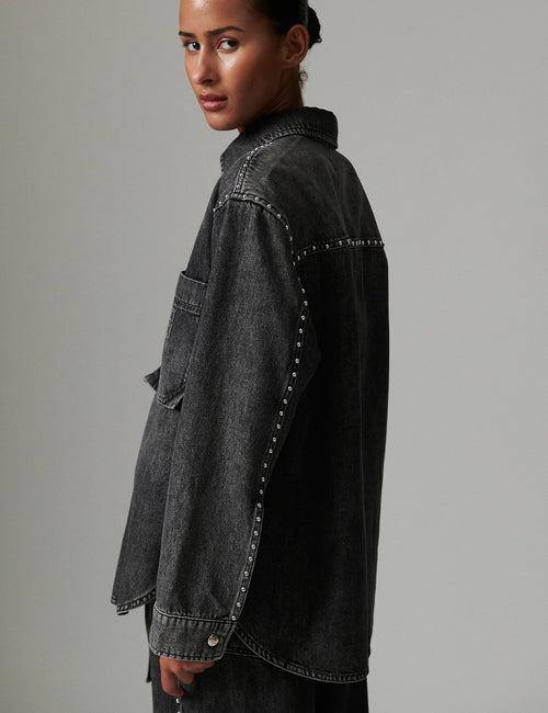 Person wearing a black denim jacket on a gray background