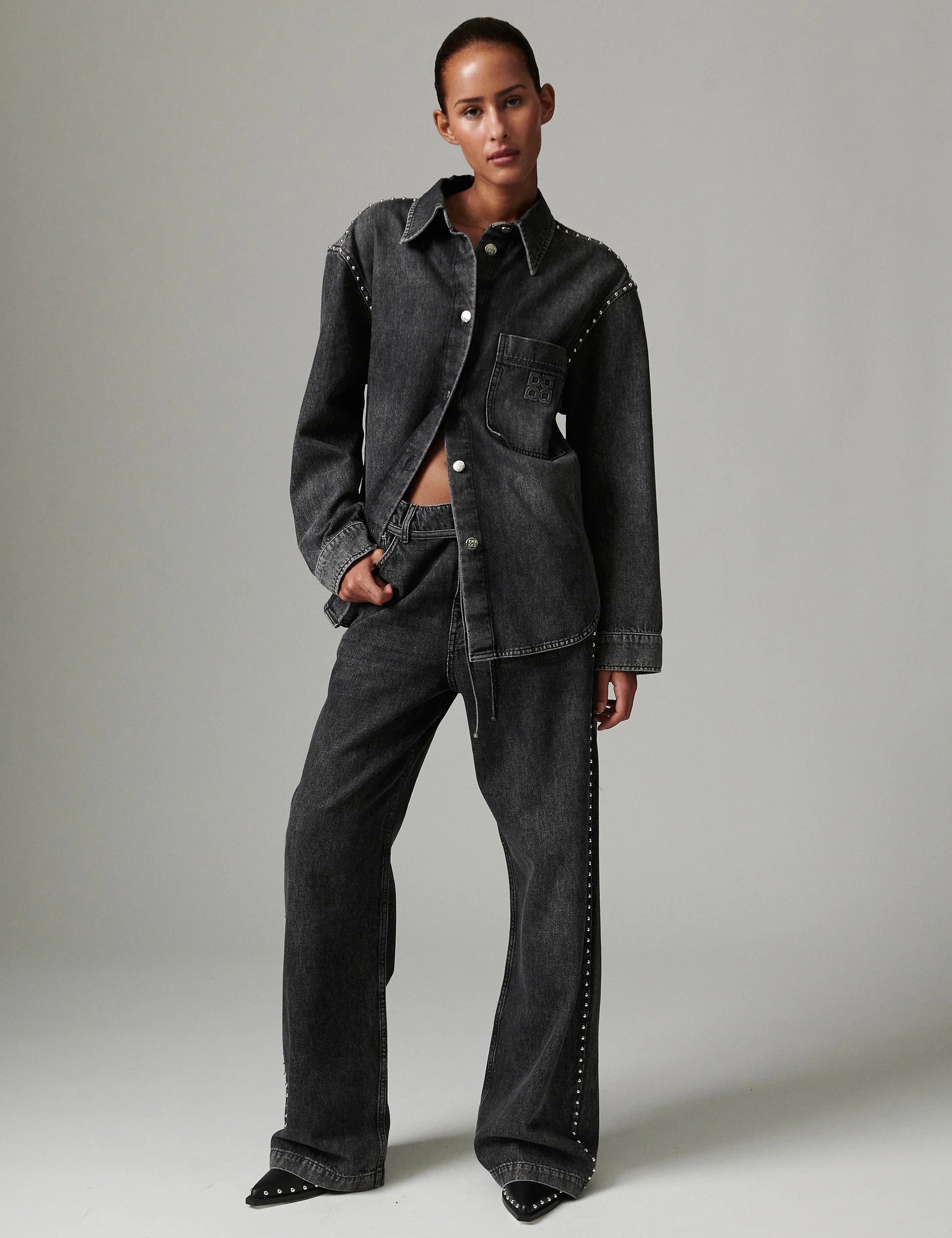 Person wearing a dark denim jacket and jeans on a plain background