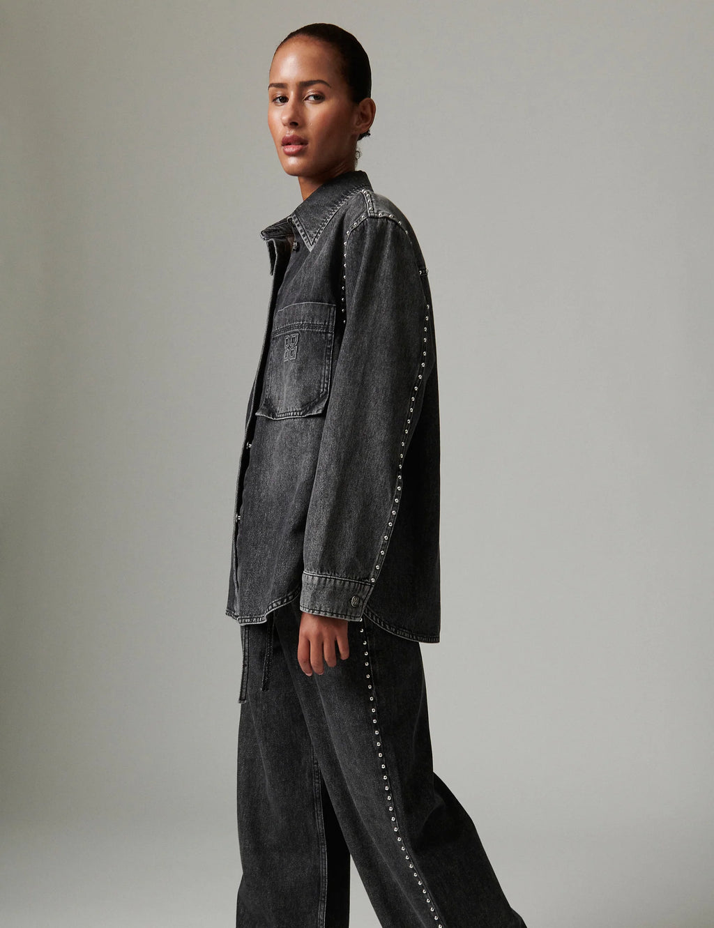 Person wearing a dark denim jacket with studded details on a plain background