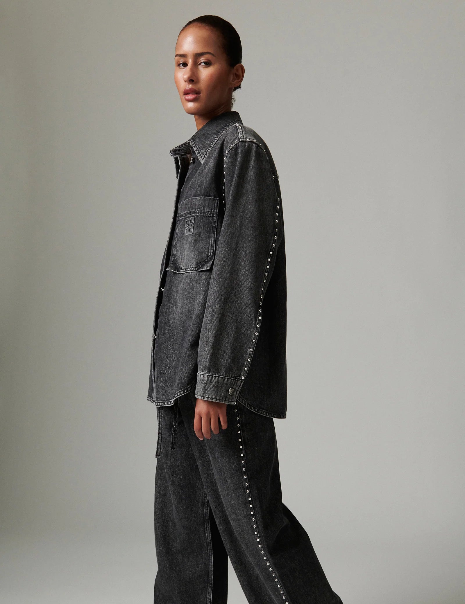 Person wearing a dark denim jacket with studded details on a plain background