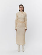 A woman standing wearing a beige maxi dress with sequins and a high neck.