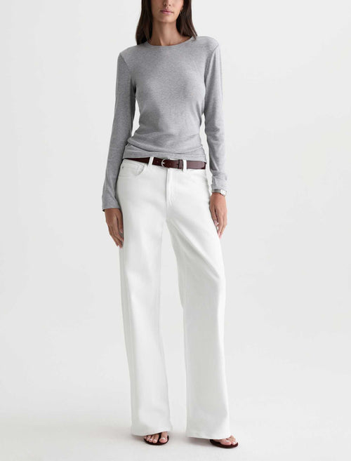 A model wearing a light gray long-sleeve knit top, white wide-leg trousers, and a brown leather belt, standing against a plain white studio background.
