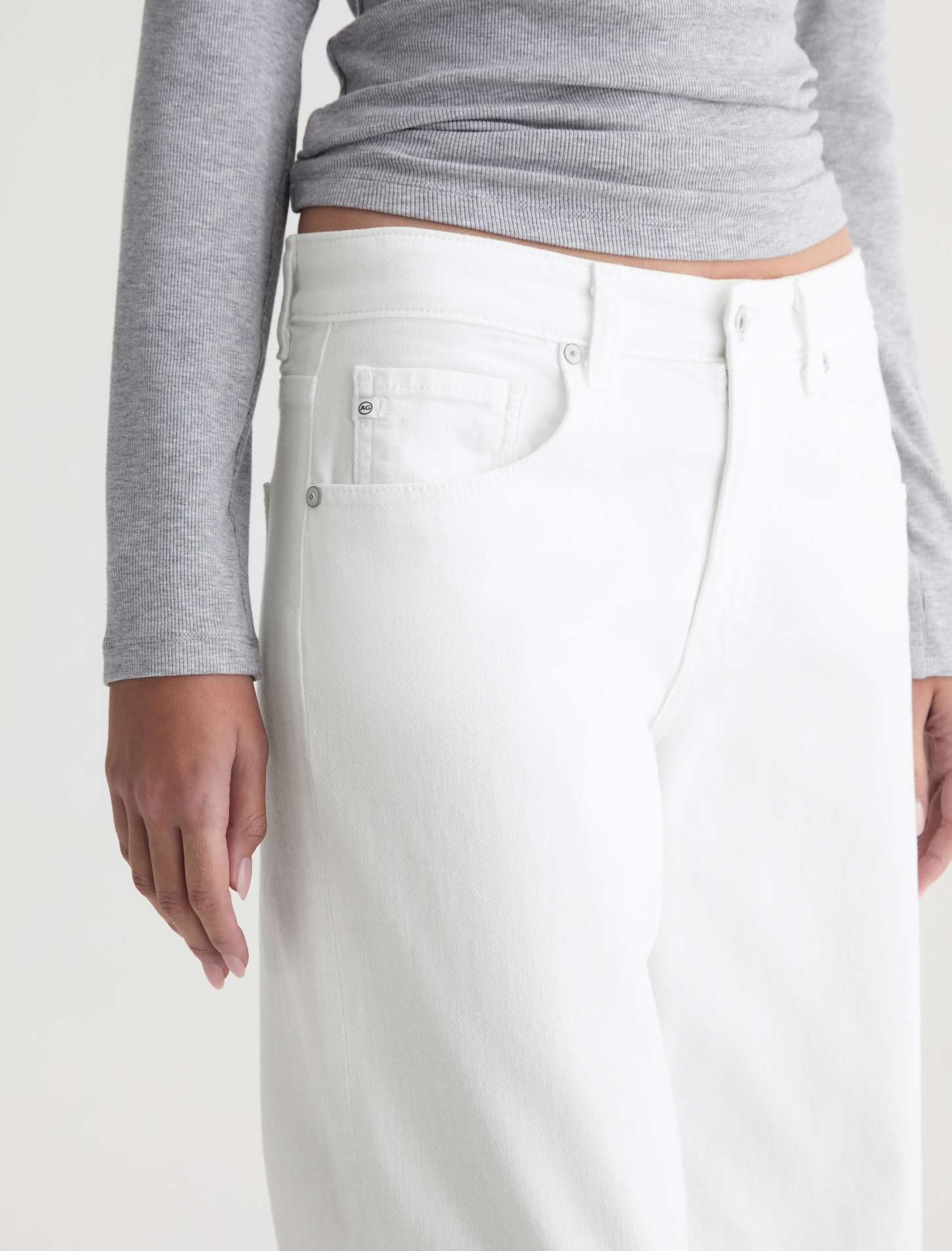 Person wearing a gray long-sleeve top and white pants on a plain background